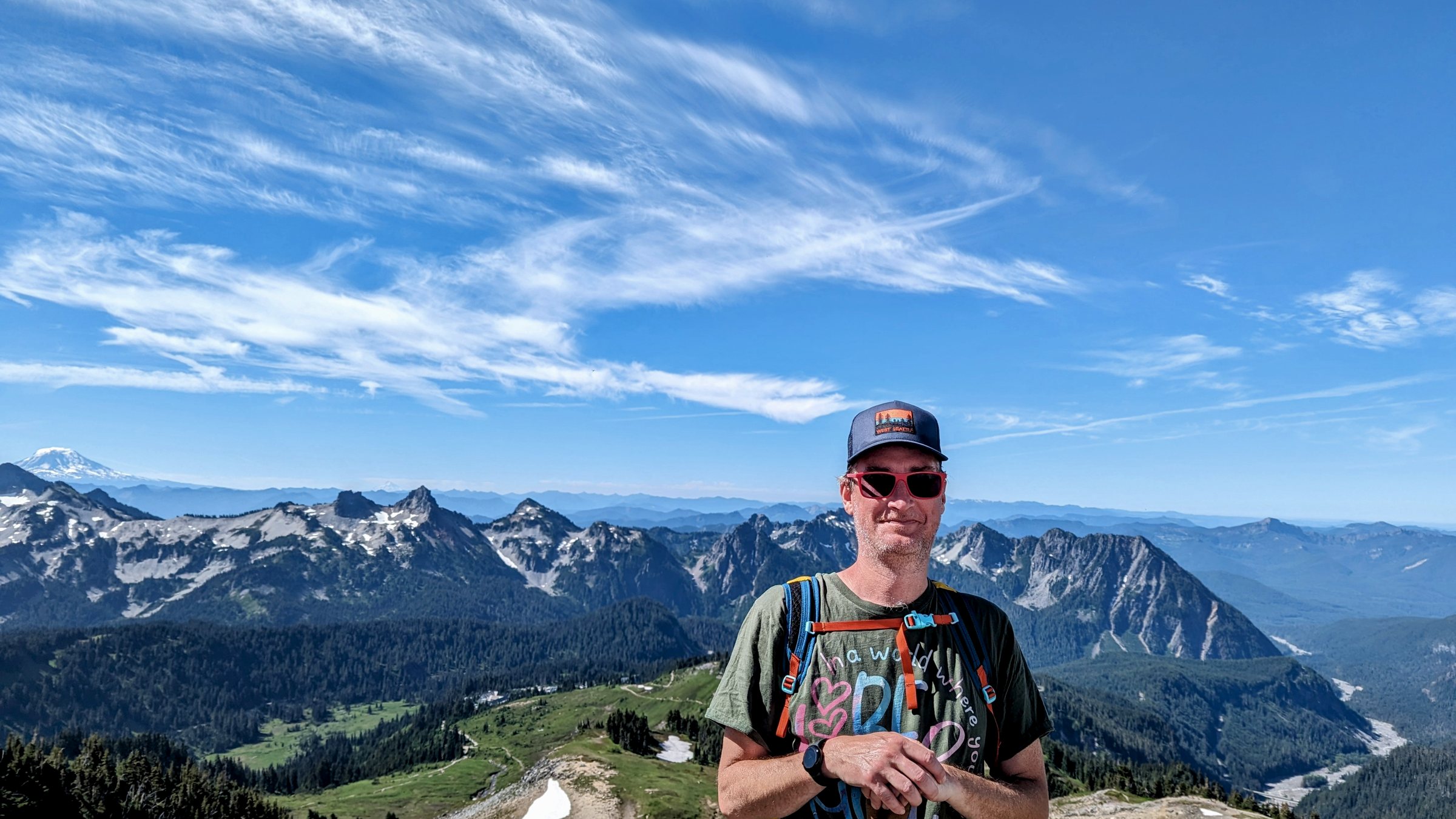 Jacob Dixon standing on a ridge in Mount Rainier National Park, the Tatoosh Range and a distant volcano behind him.